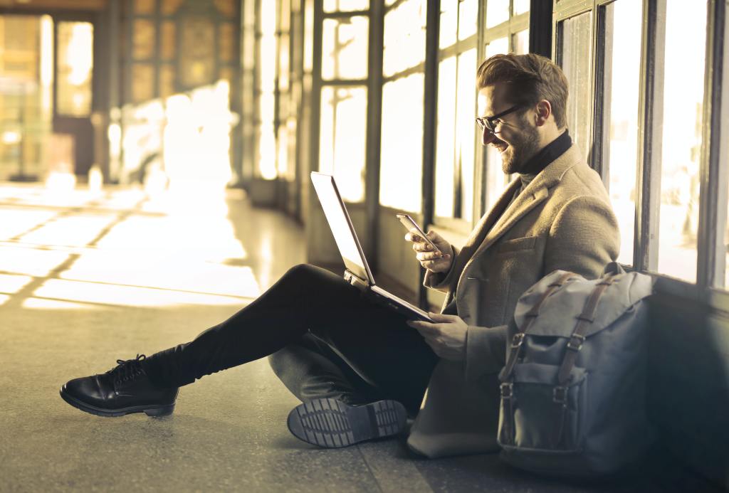 businessman sitting on airport floor using laptop and cell phone